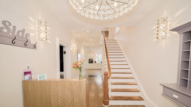 A wooden reception desk with a sign that reads "Side," a staircase with wooden steps and a white handrail, and a chandelier with multiple lights.