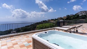 A rooftop terrace with a hot tub, lounge chairs, and a scenic view of a coastal town. - Le Arcate Giuliana by Feeling Italy (Massa Lubrense)