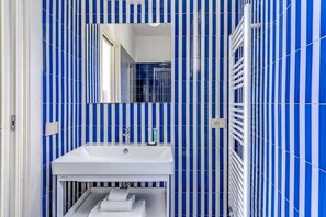 Une salle de bain avec des carreaux bleus et blancs disposés en rayures, un lavabo blanc et un miroir.