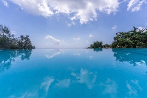 Une piscine d’un bleu éclatant, avec vue sur l’océan et bordée d’arbres de chaque côté.