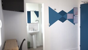 A bathroom with a sink, mirror, and a wall with geometric shapes and notices. - Relais 375 (Valence-en-Poitou)