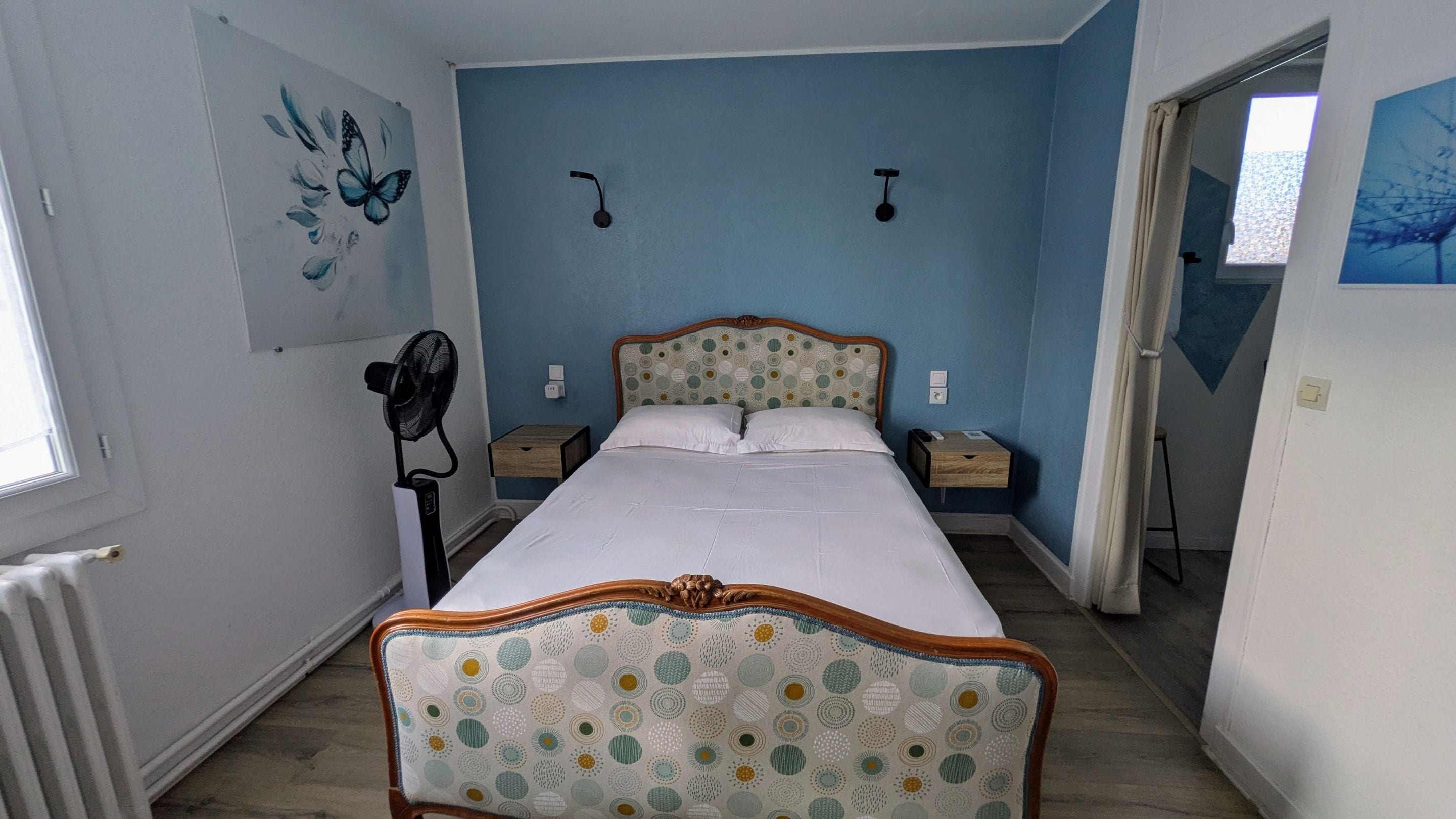 Quarto com cama, mesas de cabeceira, ventilador e janela.