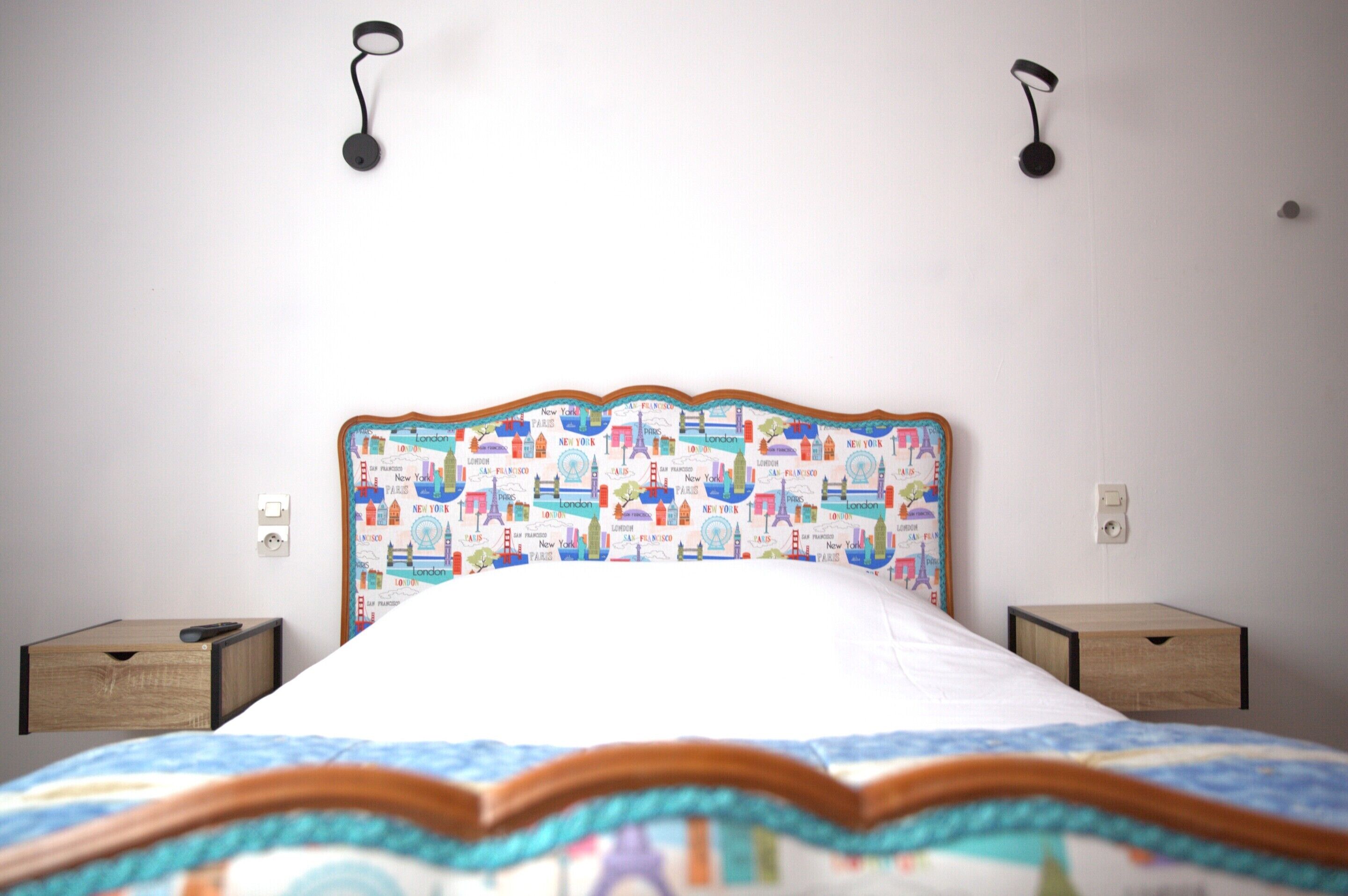 A bed with a patterned headboard, two bedside tables, and wall-mounted lamps.