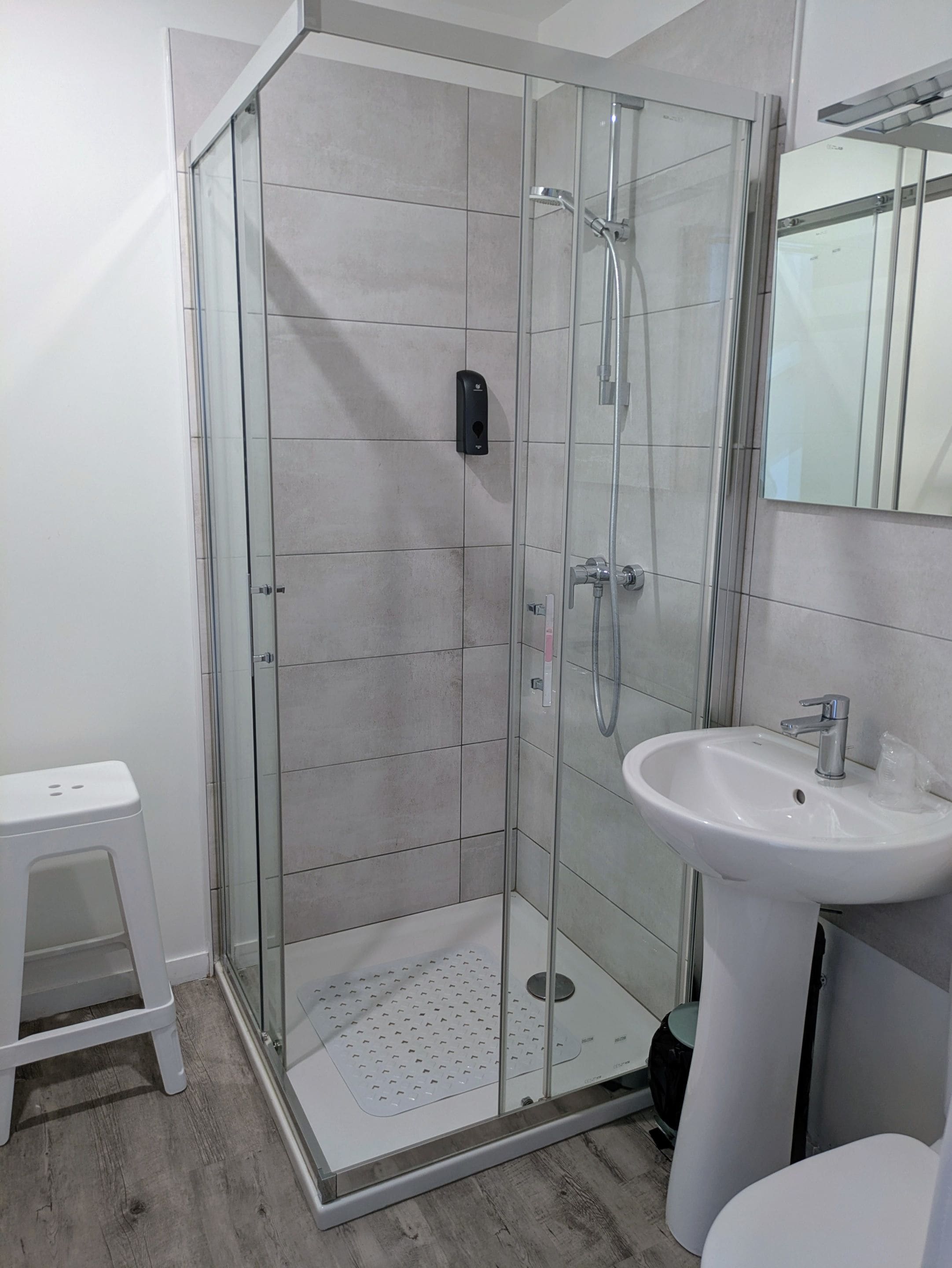 A modern bathroom with a glass-enclosed shower, a white sink, and a small stool.