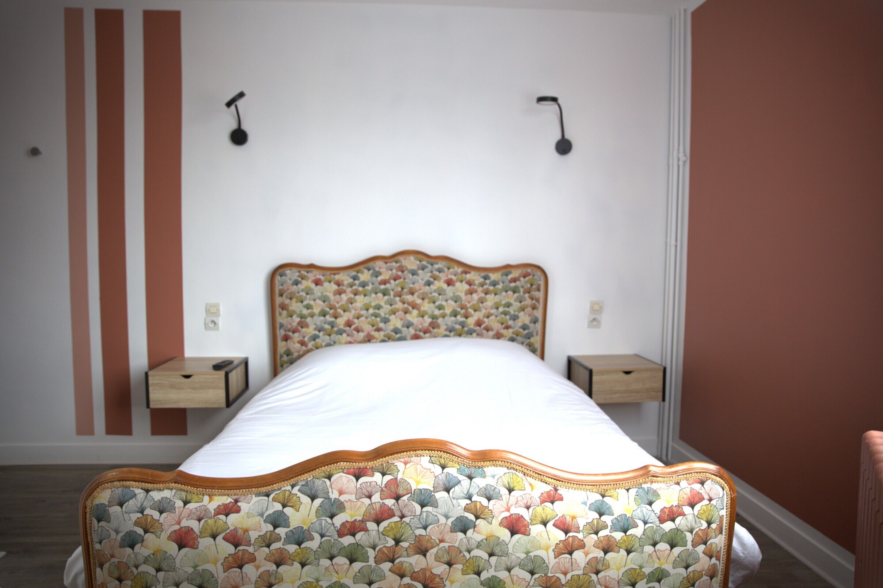 A neatly made bed with a floral-patterned headboard, two bedside tables, and a wall with vertical stripes and a hanging light fixture.