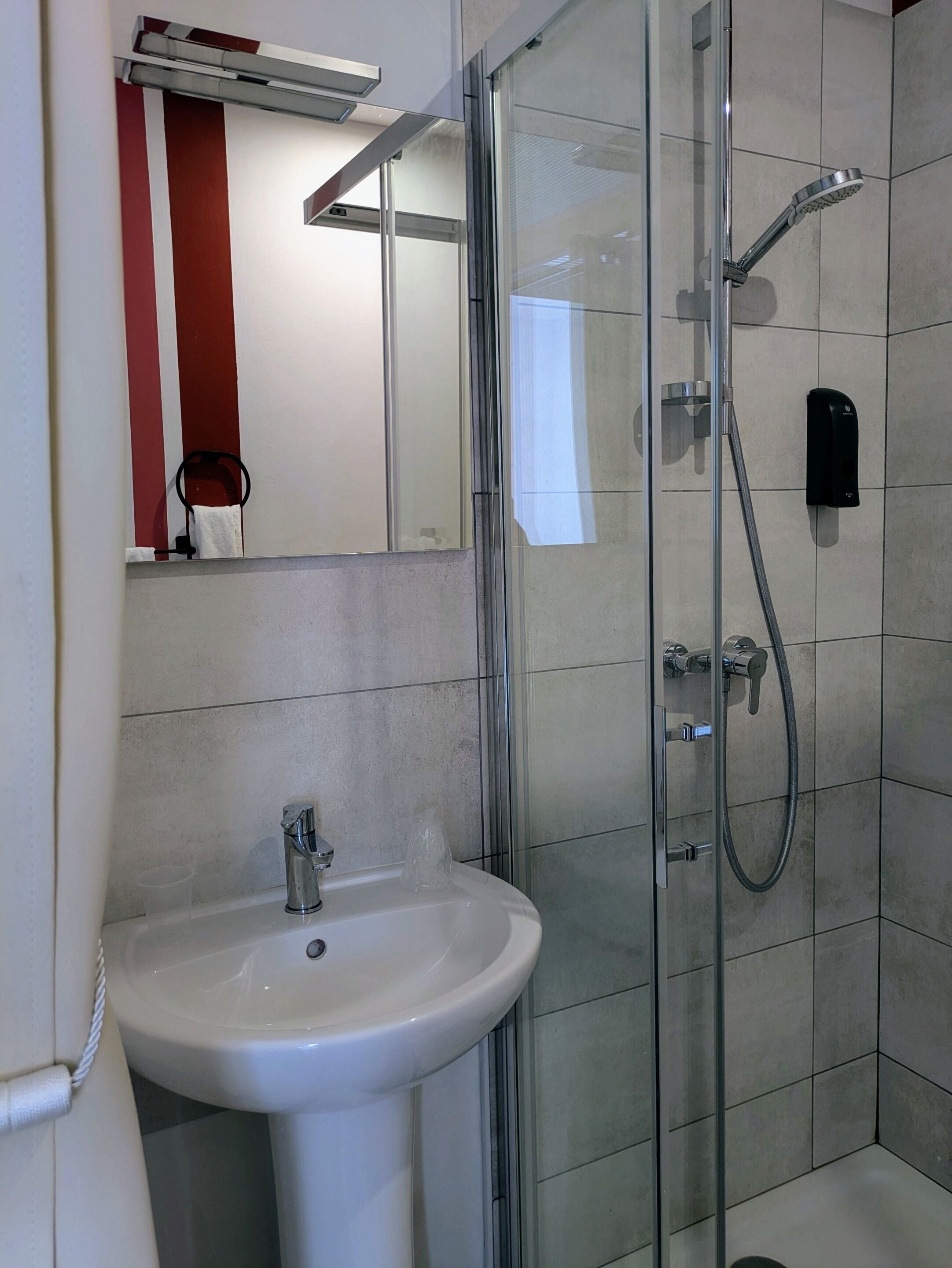 A modern bathroom with a glass shower enclosure, a white sink, and a handheld showerhead.