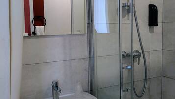 A modern bathroom with a glass shower enclosure, a white sink, and a handheld showerhead.