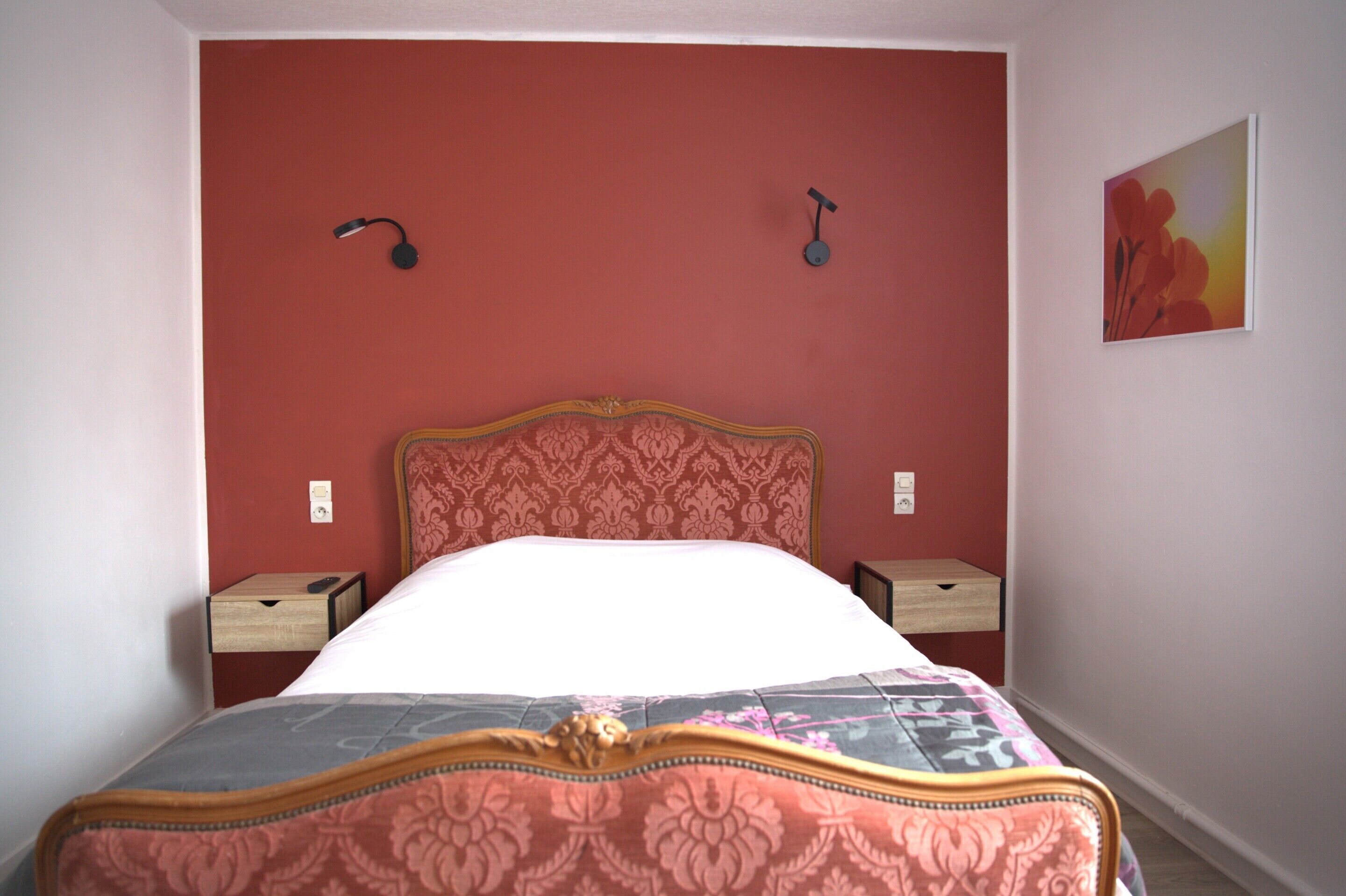 Una cama con cabecera estampada con motivos florales, dos mesitas de noche y una lámpara de pared.