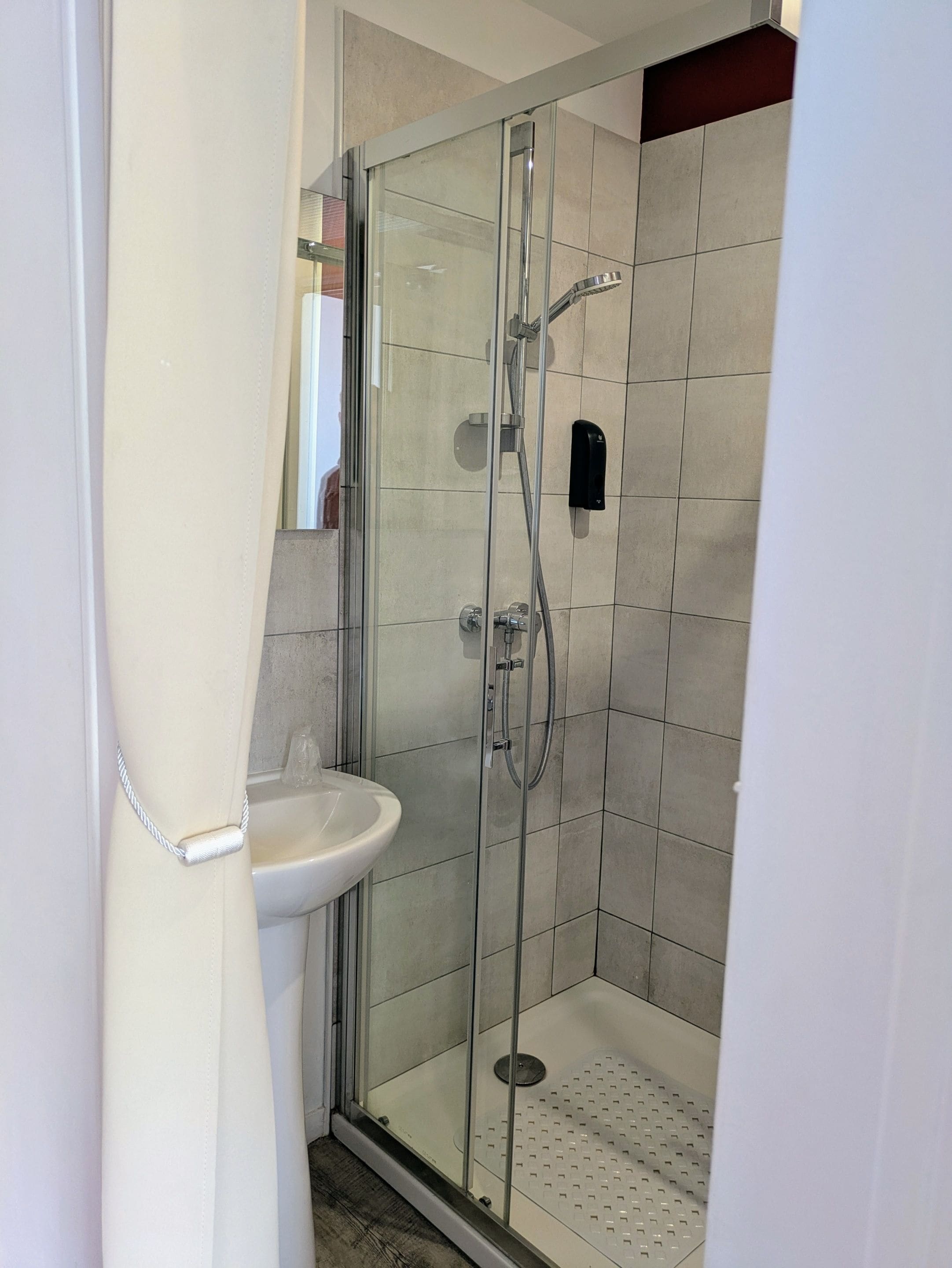 A glass-enclosed shower with a handheld showerhead and a wall-mounted faucet.