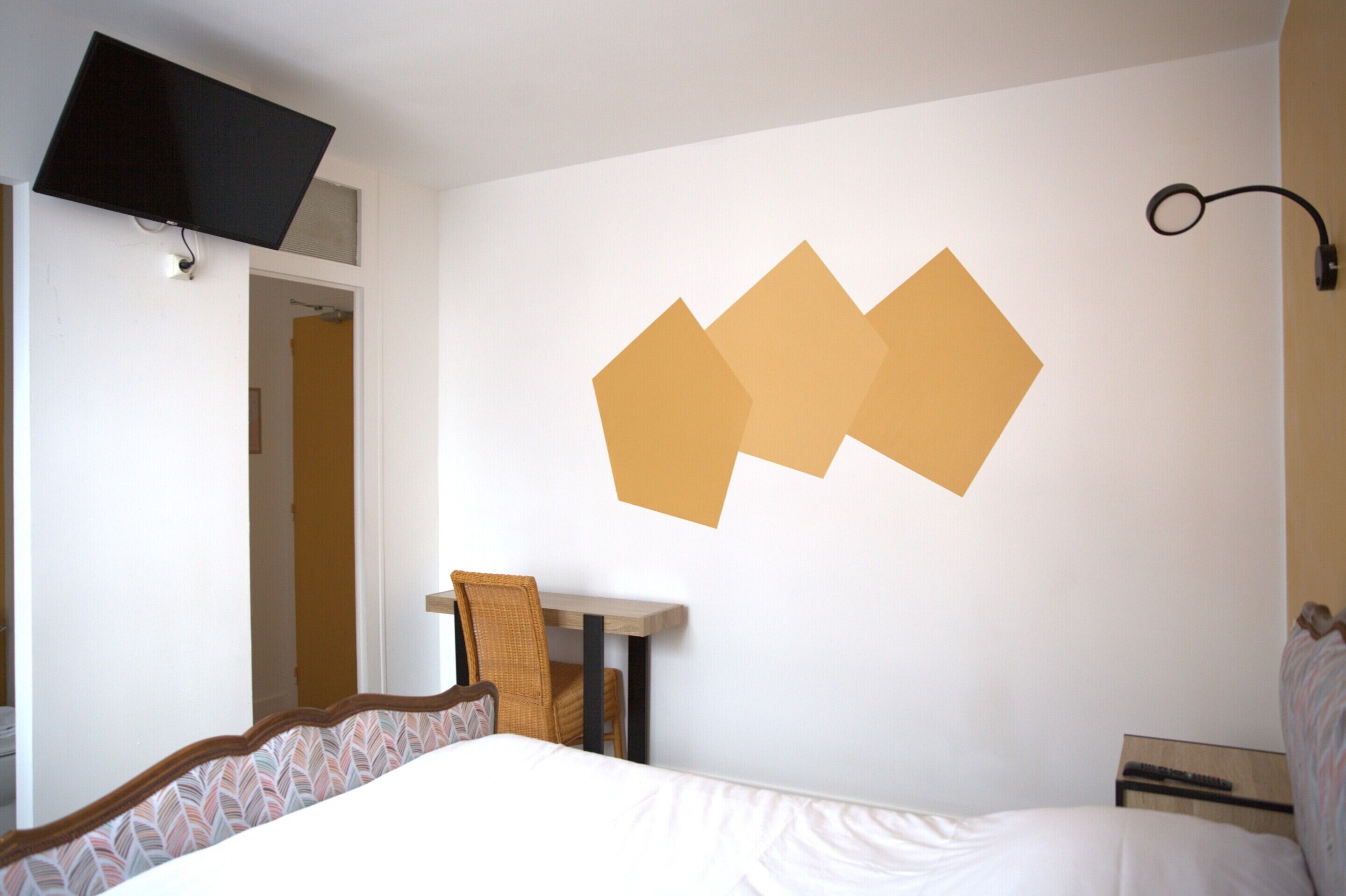 A hotel room with a bed, a desk, and a wall-mounted TV.
