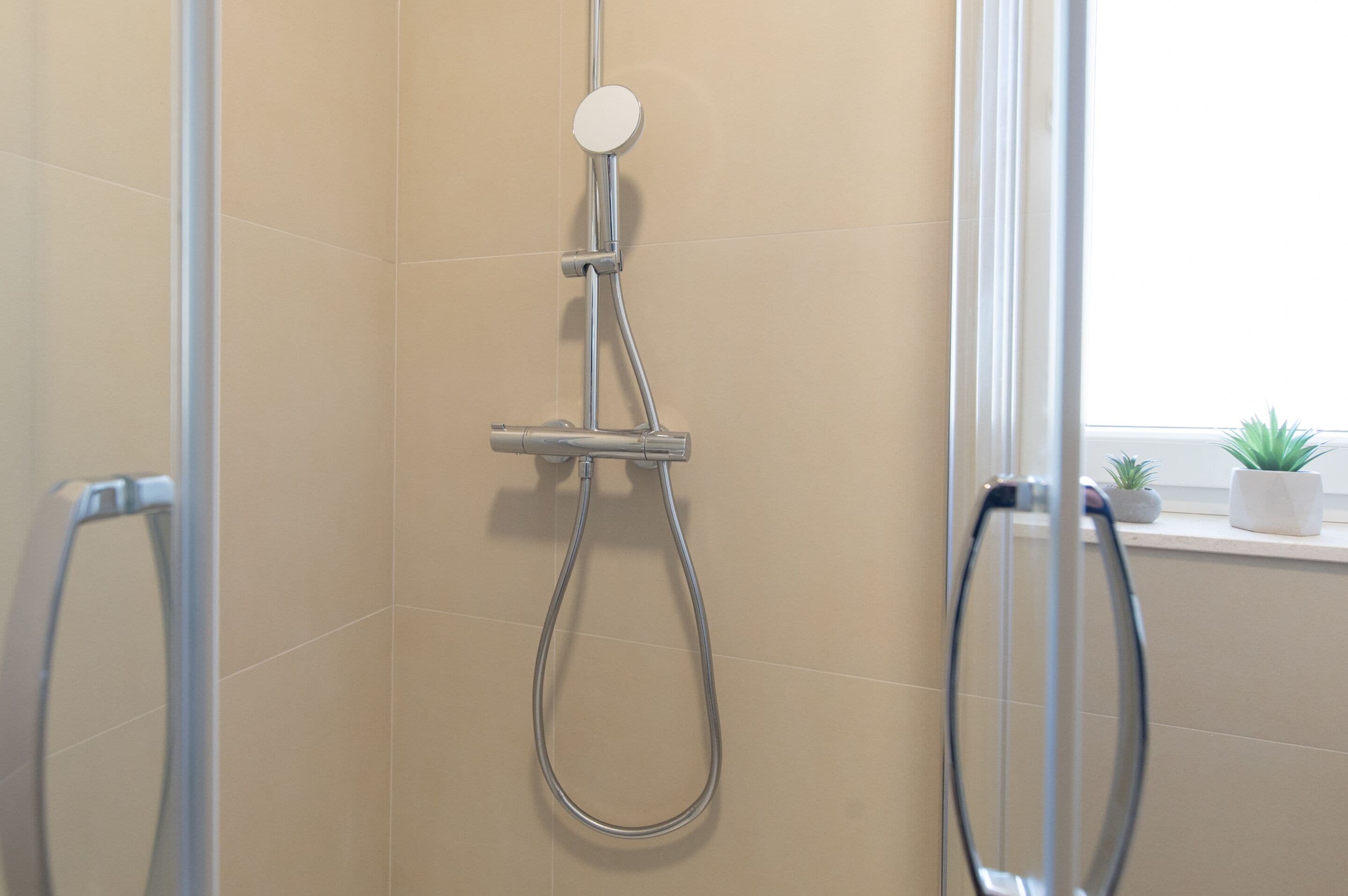A shower with a handheld showerhead and a wall-mounted control panel.