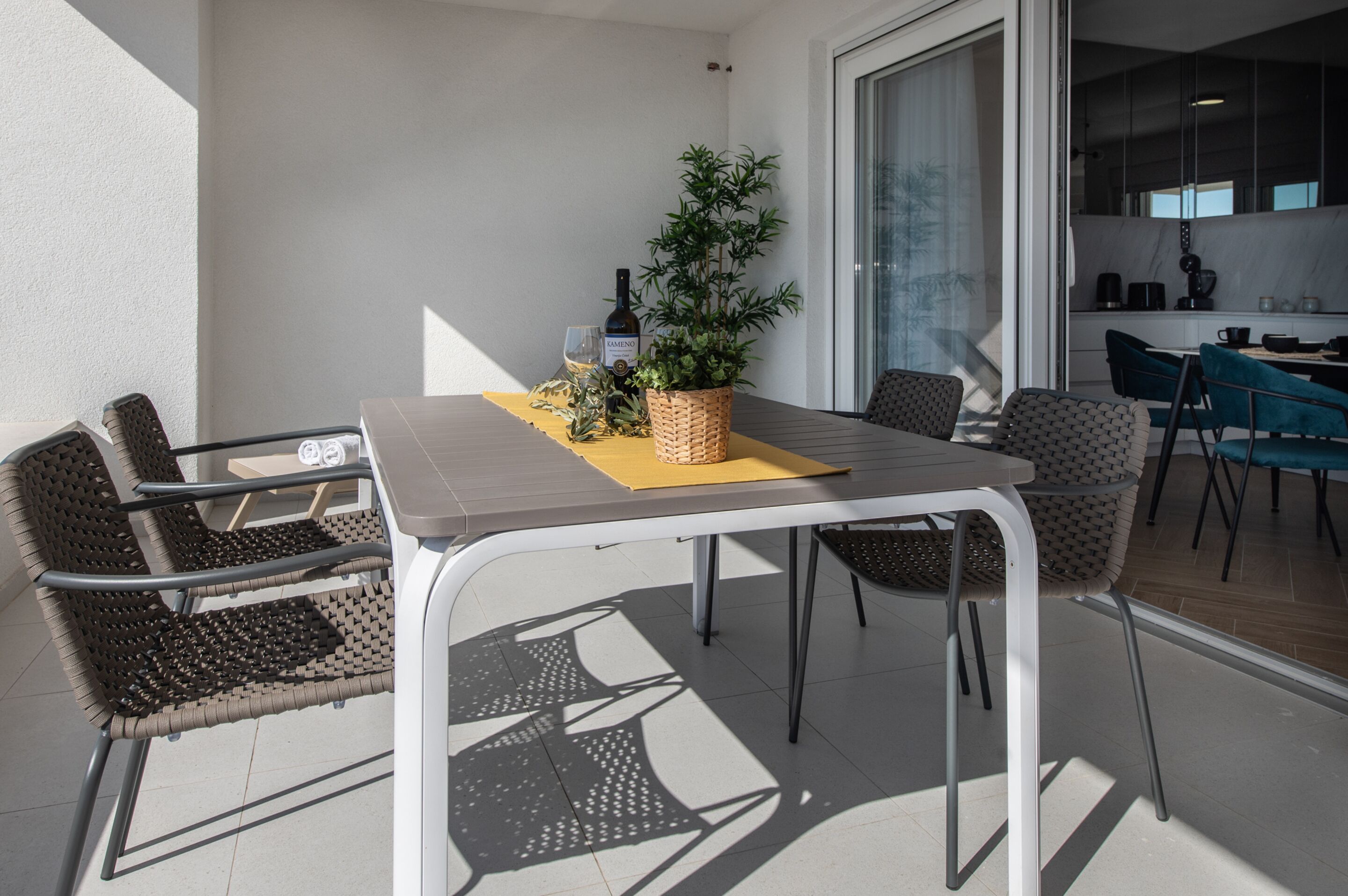 A dining area with a table, chairs, a potted plant, and a bottle of wine.