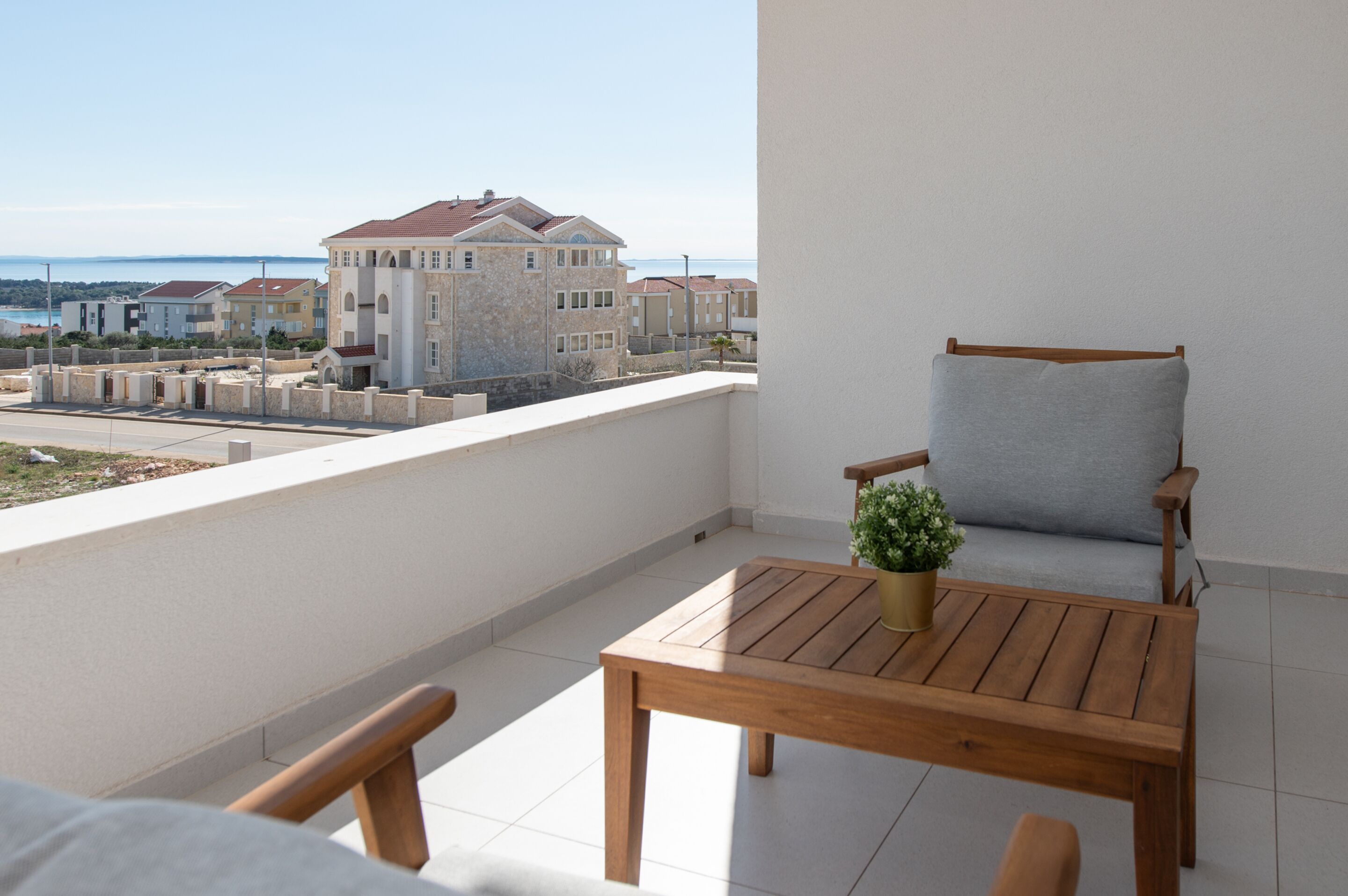 Un balcon avec une table et une chaise en bois, un pot de fleurs et une vue sur les bâtiments et la mer.