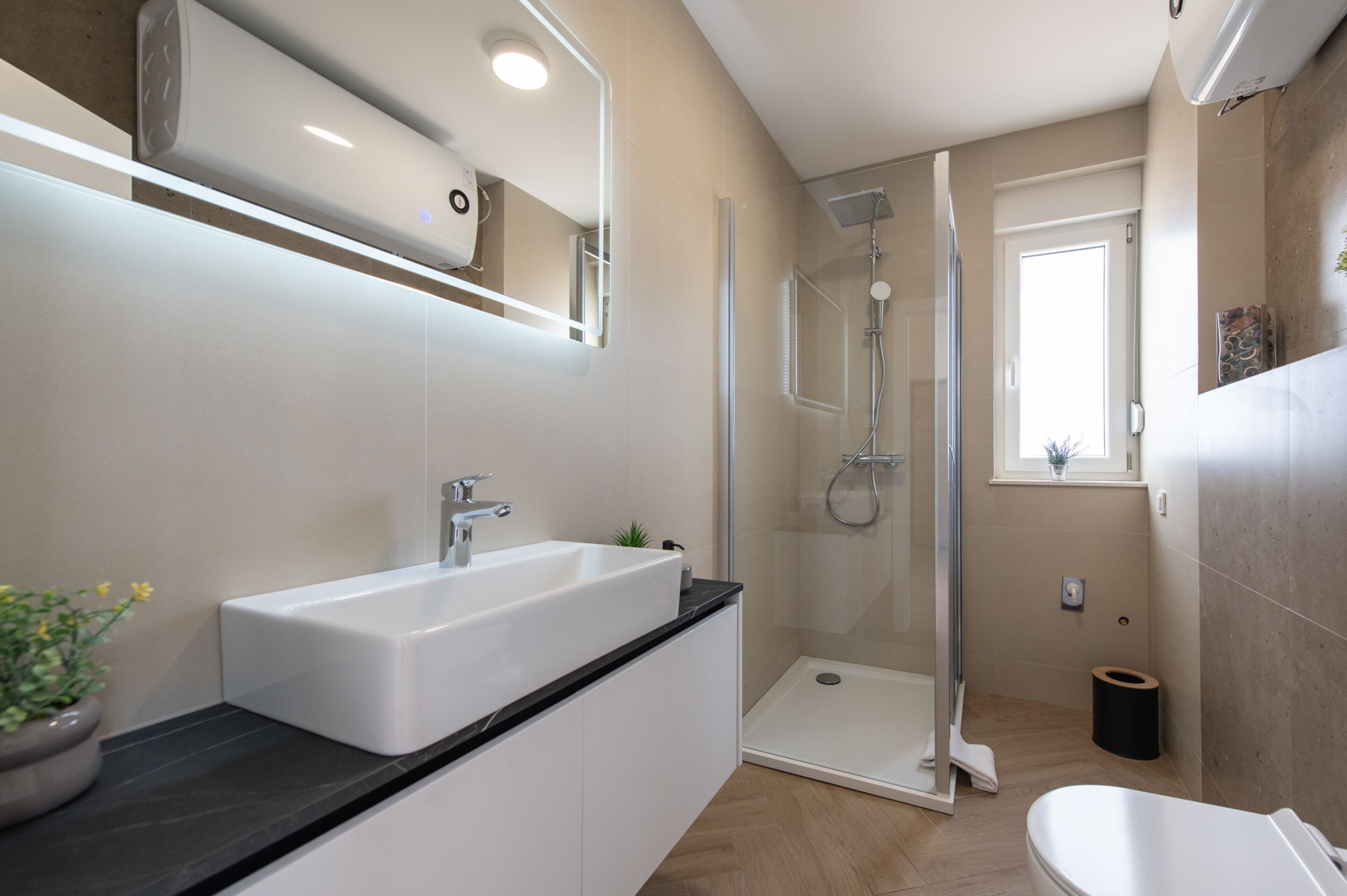 Un bagno moderno con un lavandino bianco, uno spazio doccia in vetro e un water.