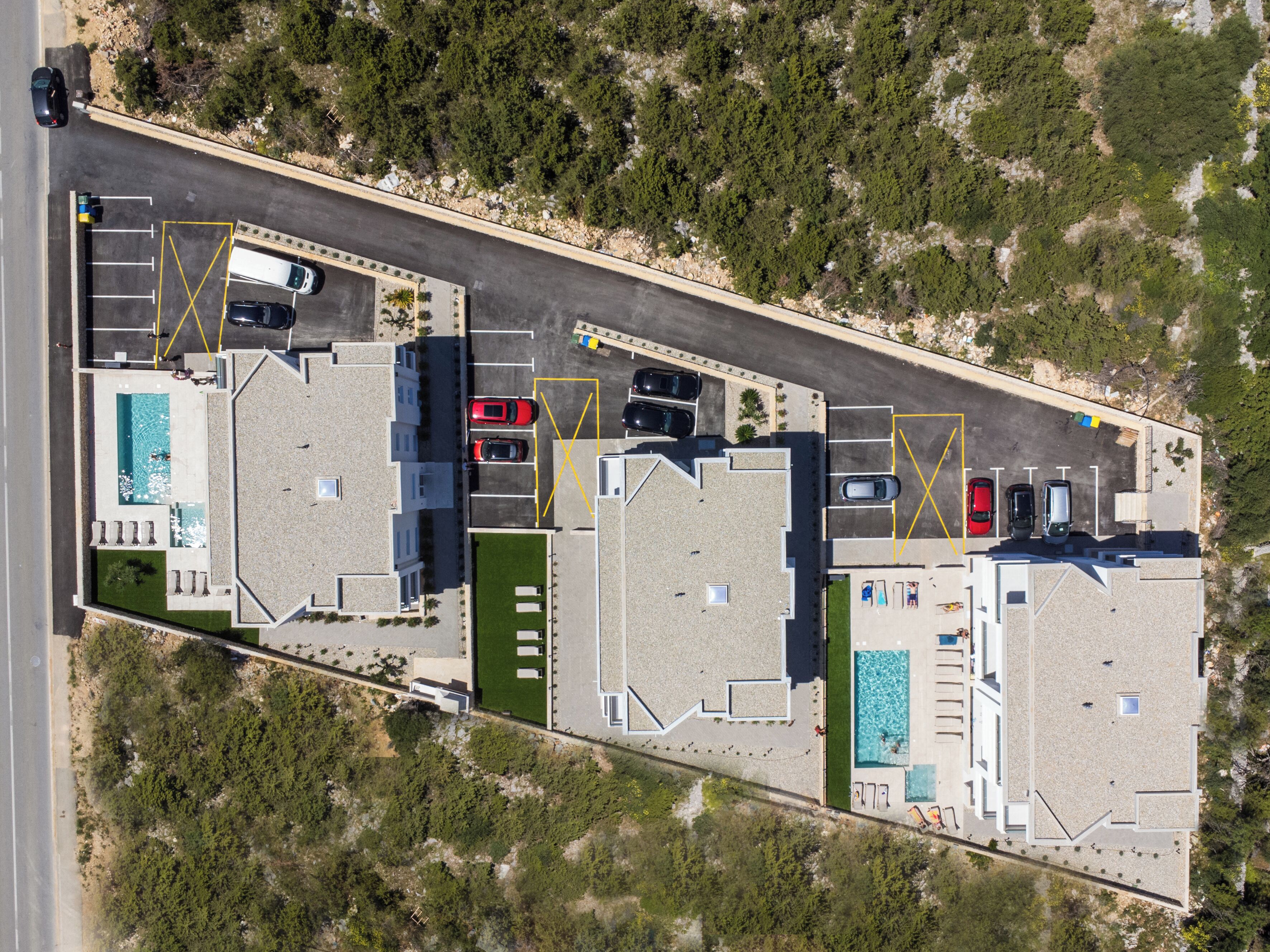 An aerial view of a hotel with multiple swimming pools, parking spaces, and a road adjacent to the property.