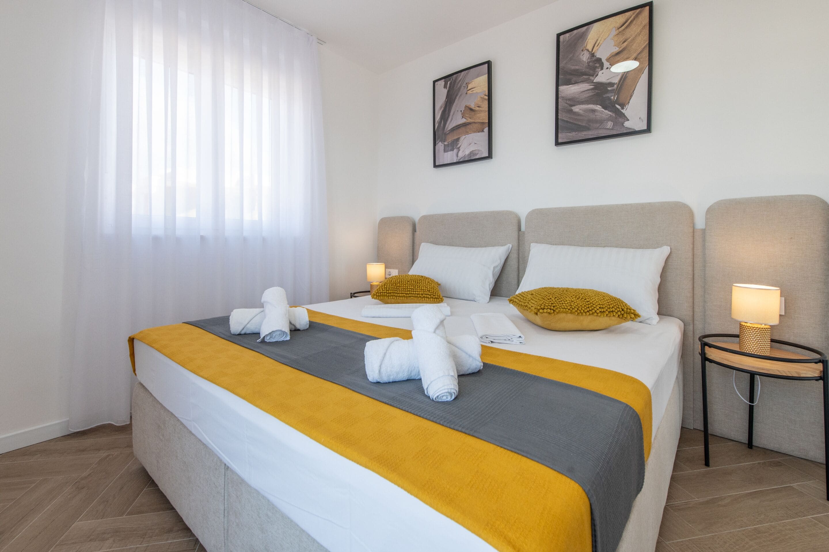 A hotel room with a large bed, two bedside tables, and a window with sheer curtains.