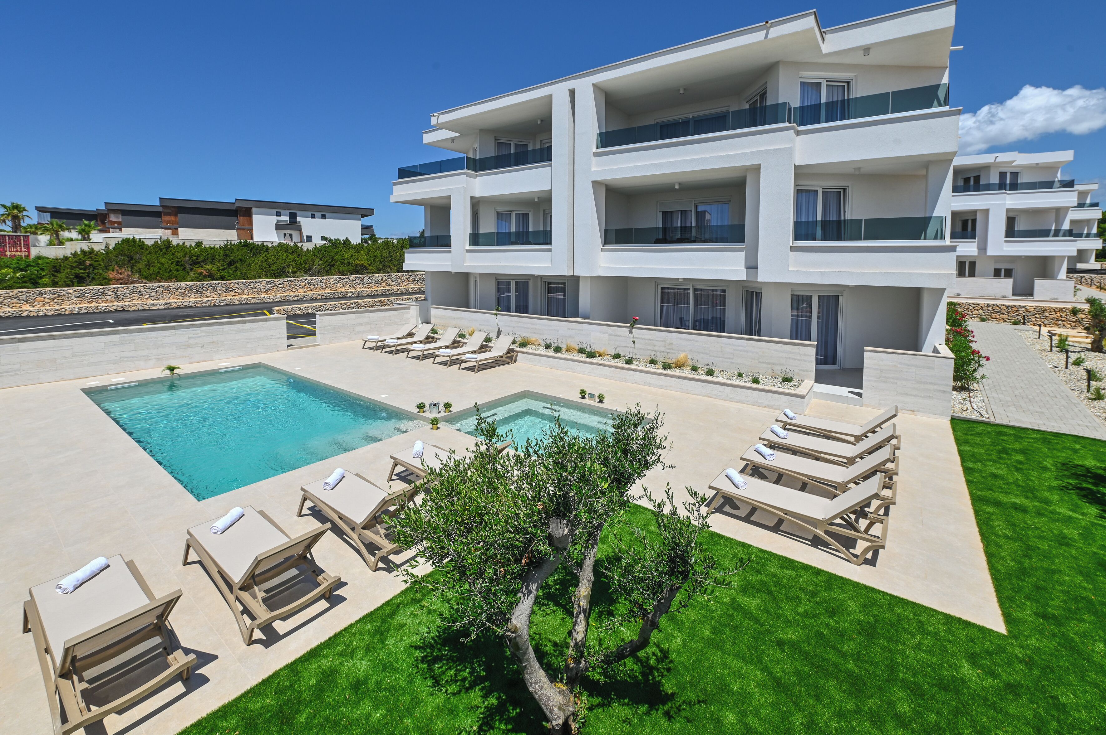 Un immeuble moderne à plusieurs étages, doté d’une piscine et de chaises longues.