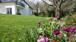 A white house with a black roof, a balcony, and a garden with tulips and other flowers.