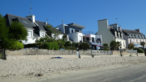 A coastal residential area with modern houses, a sandy beach, and a stone wall.