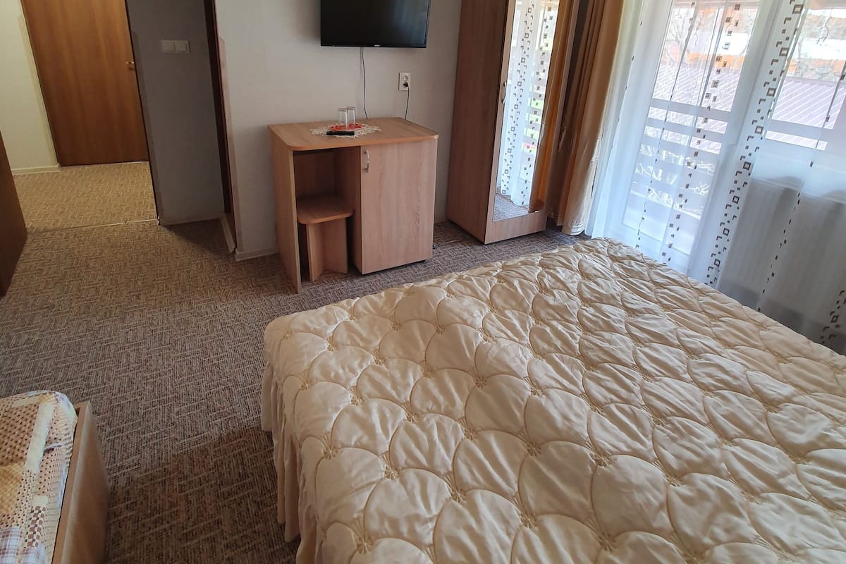 A hotel room with a large bed, a desk with a chair, a TV mounted on the wall, and a wardrobe.