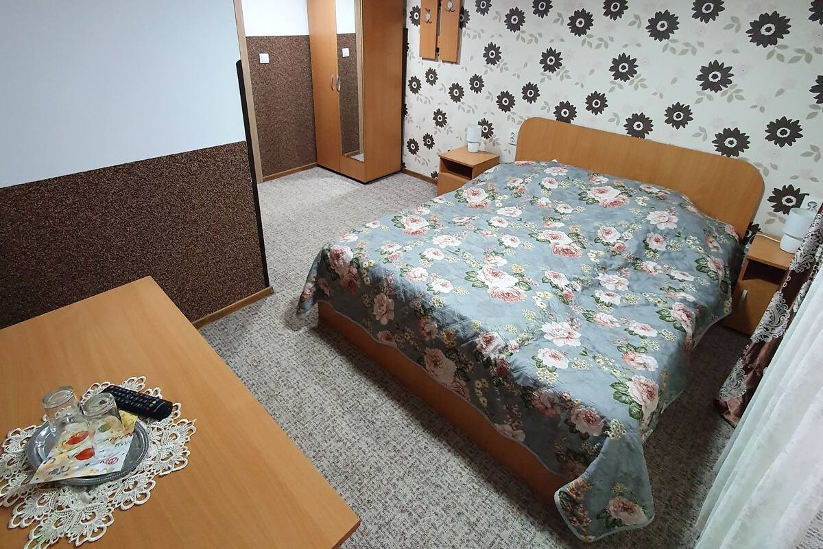 A bedroom with a bed, a wooden desk, a wardrobe, and a mirror.