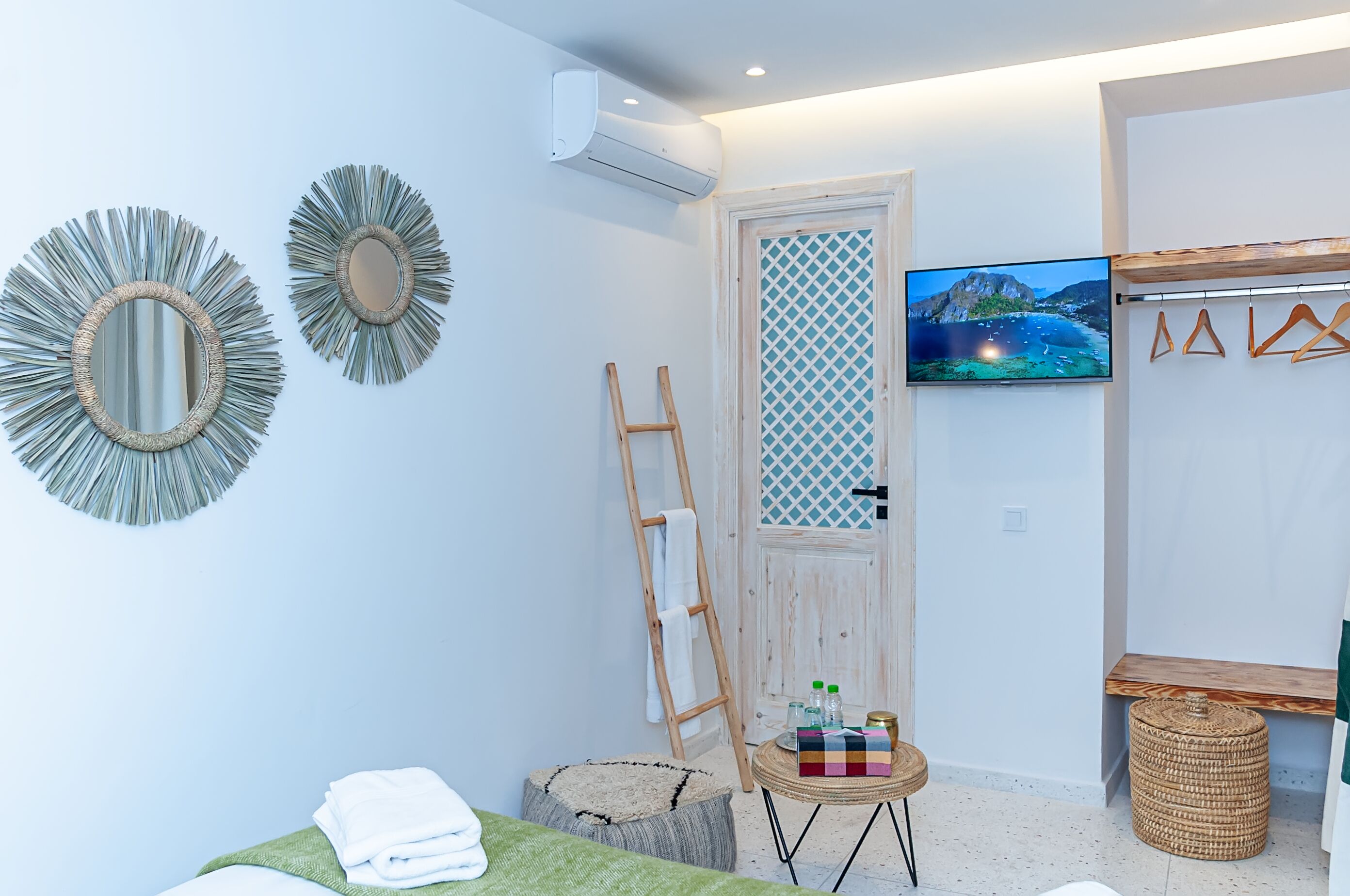 Een kamer met een bed, een televisie, een ladder en een klein tafeltje met flessen.