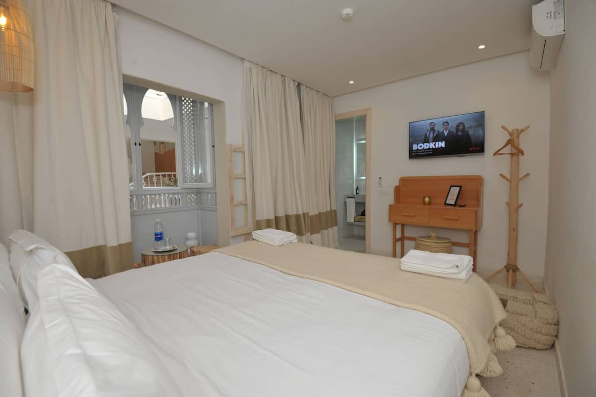Une chambre d’hôtel avec un grand lit, une télévision, une commode en bois et un miroir.