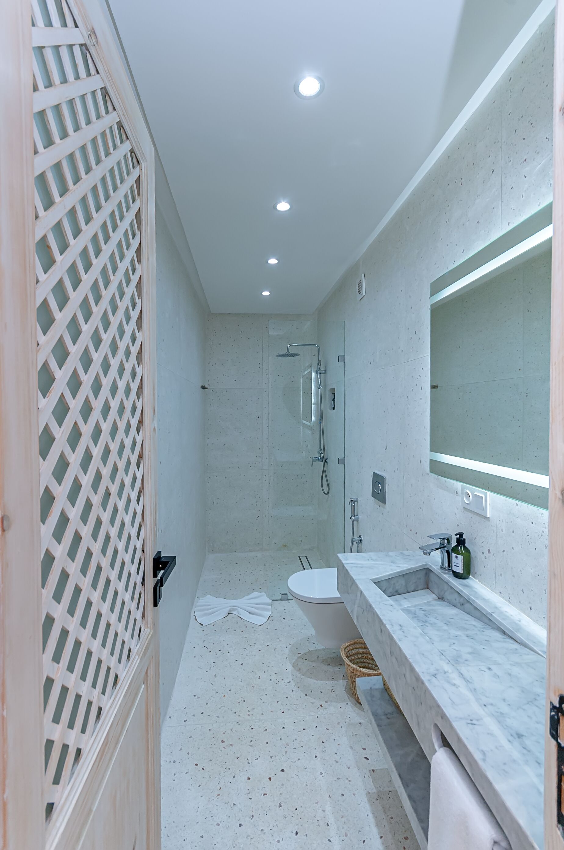 Une salle de bain moderne avec une douche, deux lavabos, un grand miroir et une porte à claustra en bois.