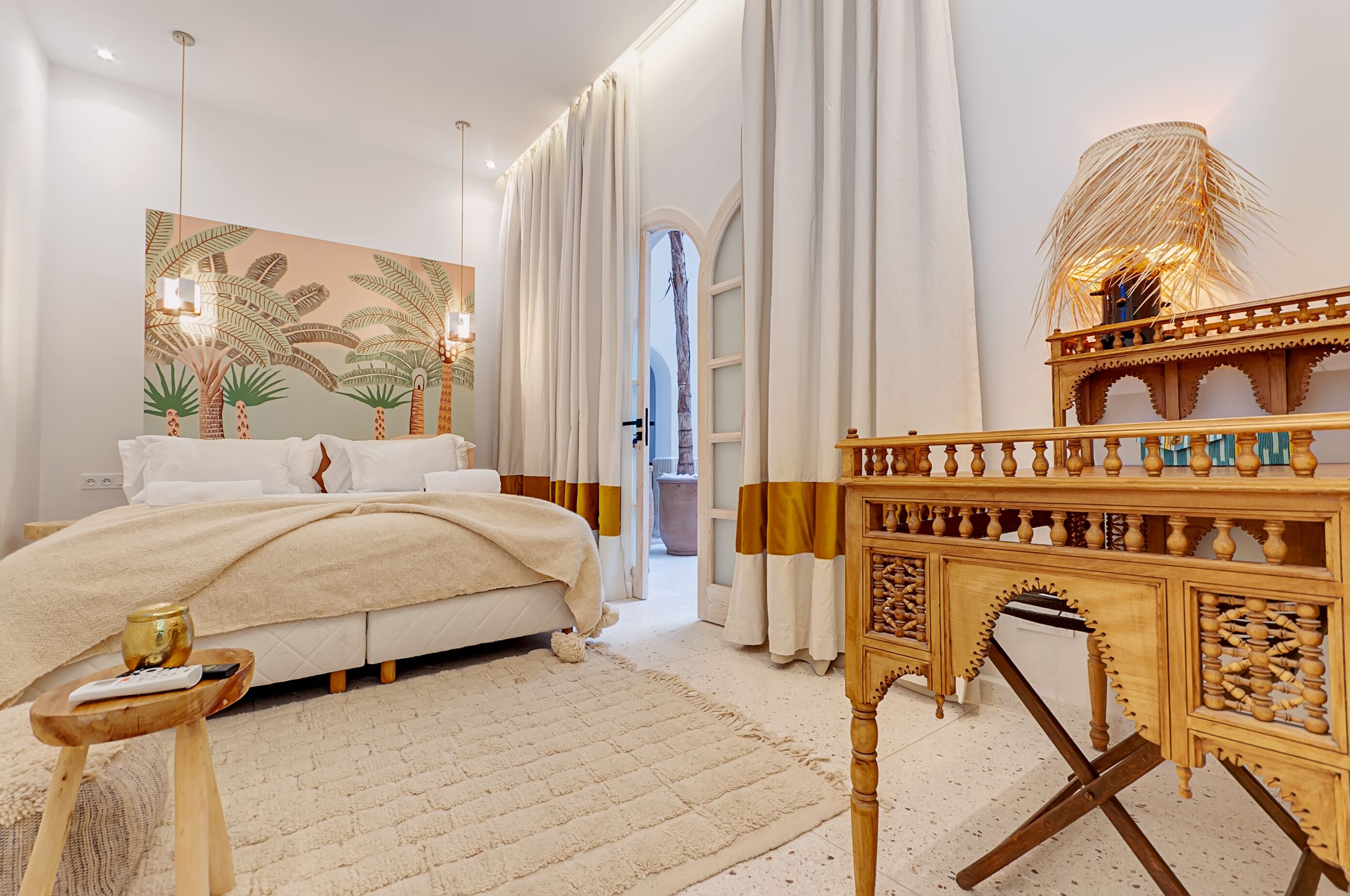 Ein Schlafzimmer mit einem Bett, einem Holznachttisch, einem großen Gemälde und Blick ins Freie.