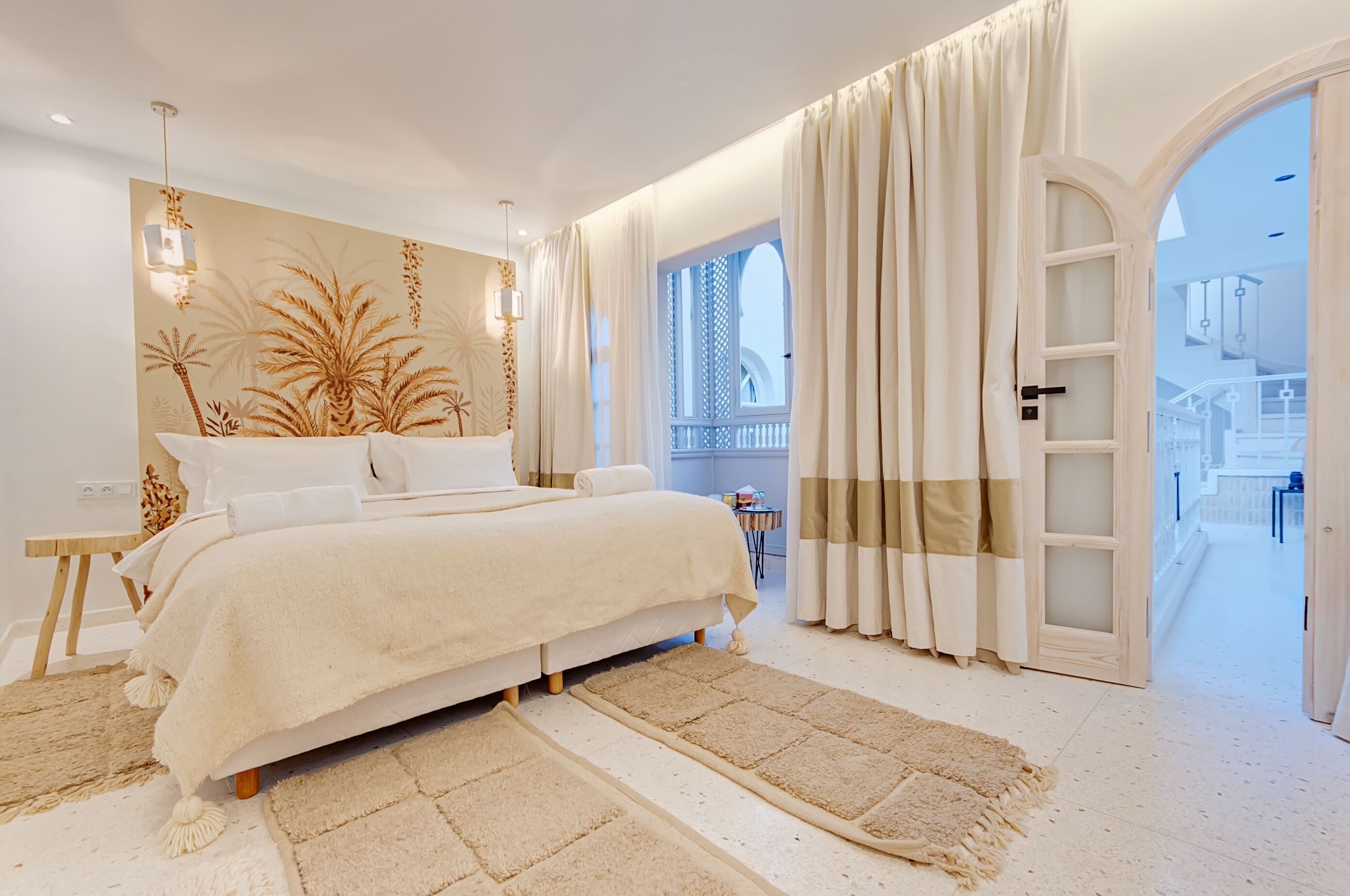 A bedroom with a large bed, a nightstand, a wall-mounted lamp, and a view of a balcony through an open door.