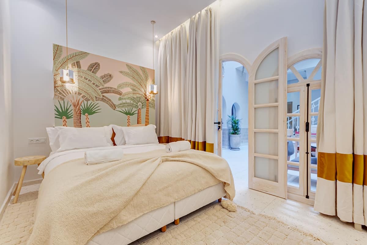 Une chambre à coucher comprenant un lit, une table de chevet, une lampe fixée au mur et une vue sur l’extérieur par une porte.