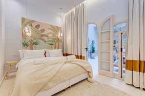 Un dormitorio con cama, mesita de noche, lámpara de pared y vistas al exterior a través de una puerta.