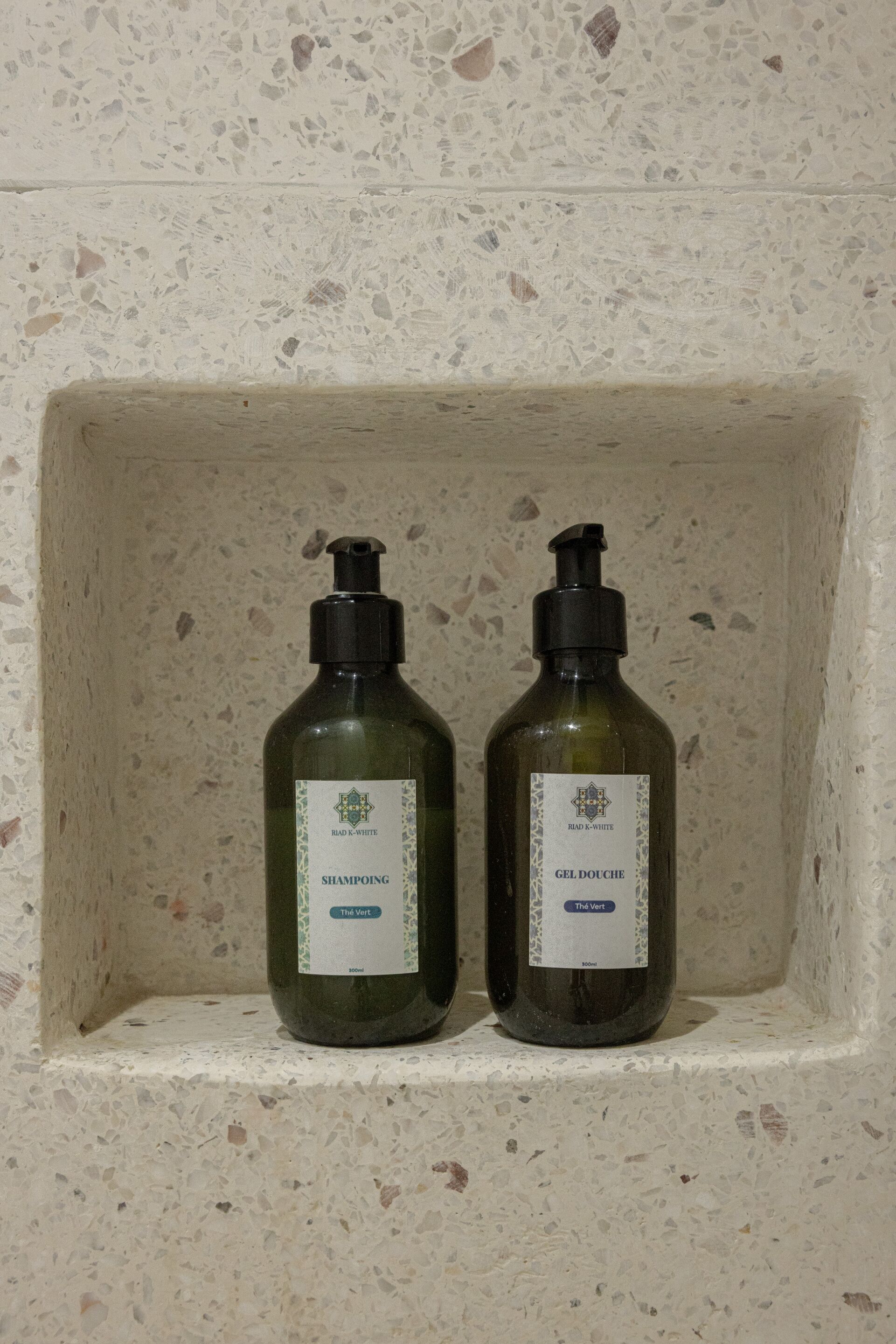 Zwei Flaschen Riad K-White Shampoo und Duschgel in einer Steinhobelbank.