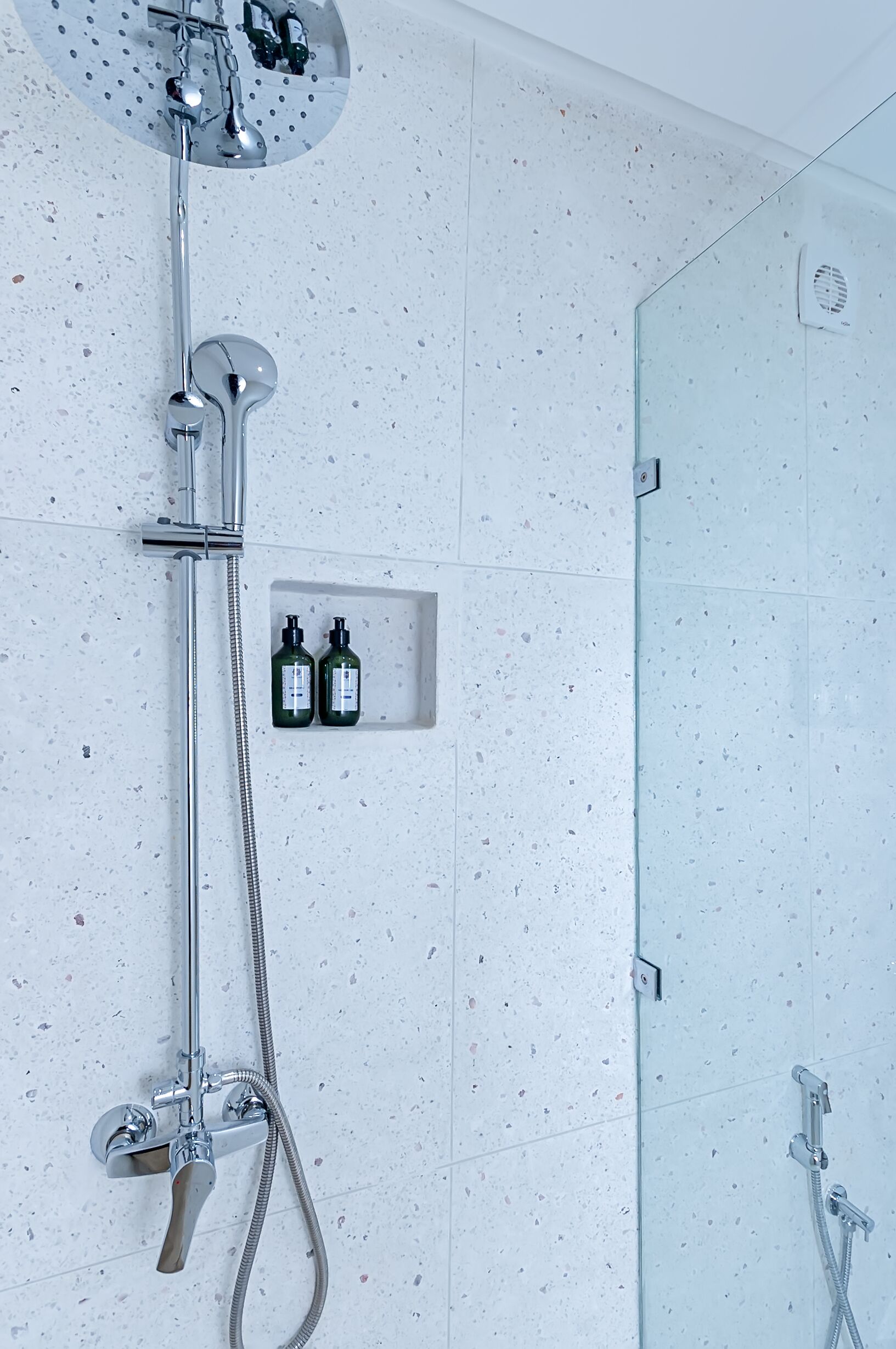 Una ducha moderna con cabezal de ducha de mano, grifo empotrado en la pared y zona de ducha con paredes de cristal.