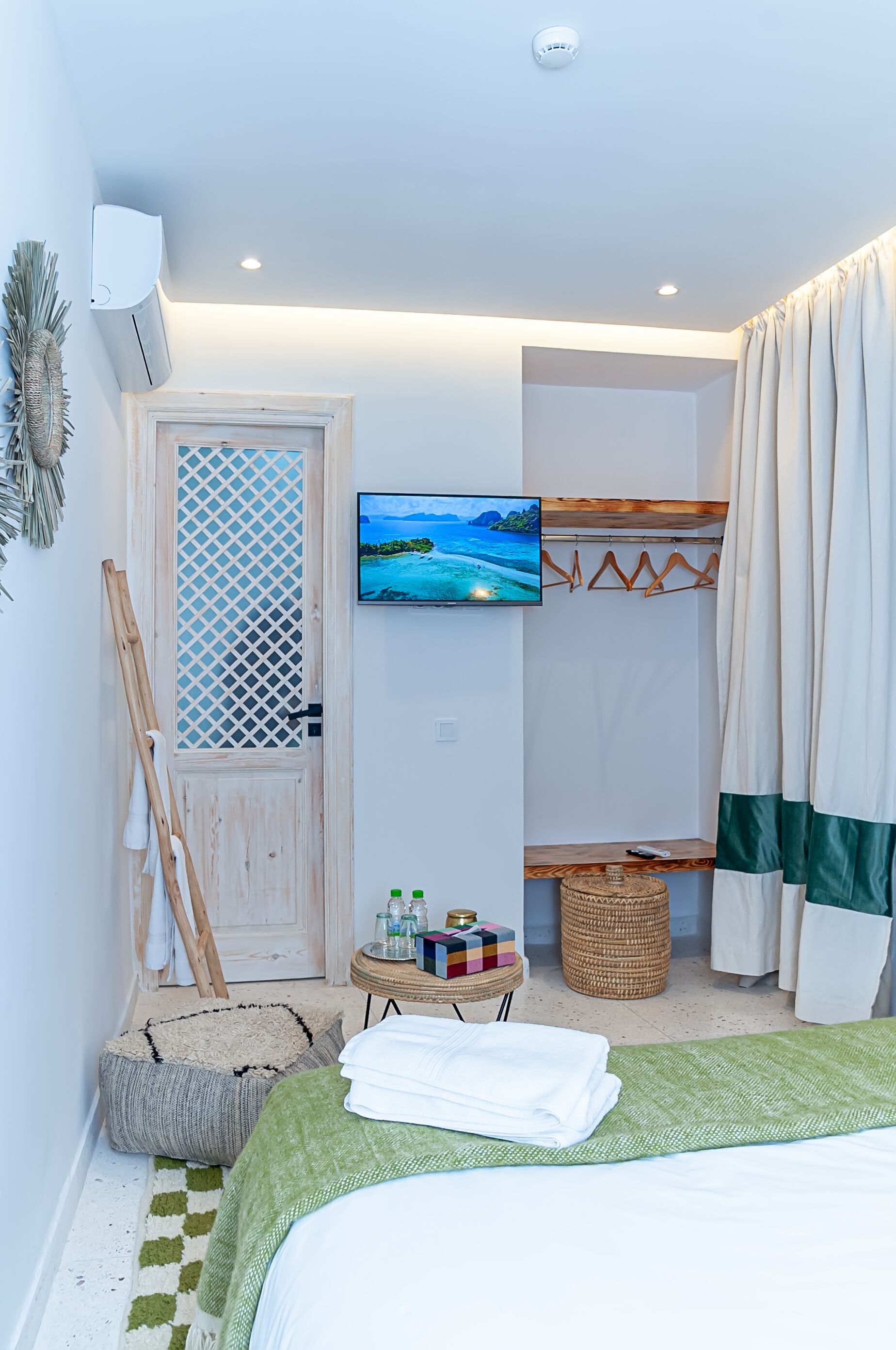 Une chambre à coucher avec un lit, une télévision, une porte en bois, une petite table avec des articles de toilette et un panier en osier.