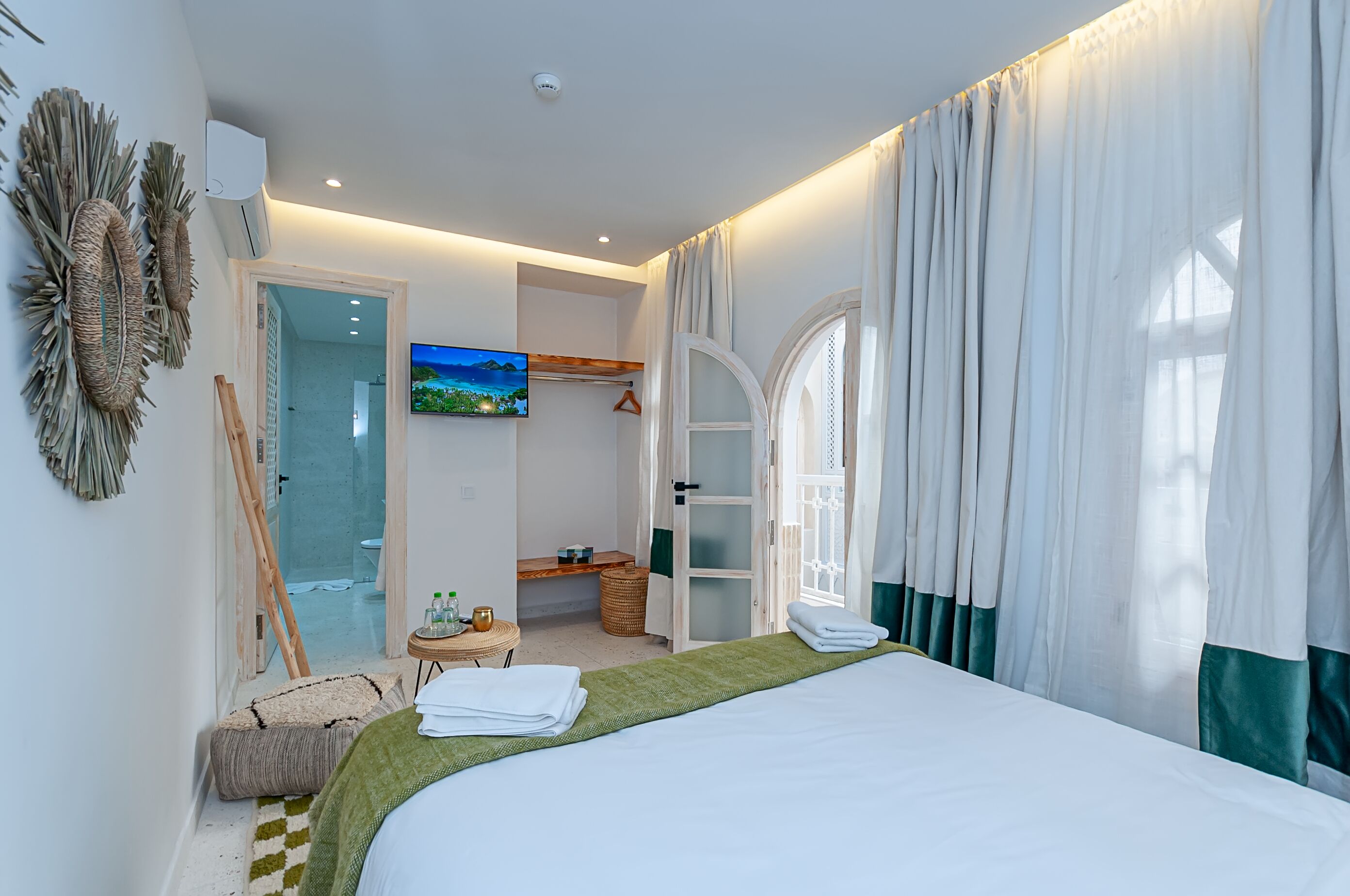 Habitación de hotel moderna con cama, televisión, armario y baño visible a través de una puerta abierta.