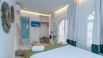 Habitación de hotel moderna con cama, televisión, armario y baño visible a través de una puerta abierta.