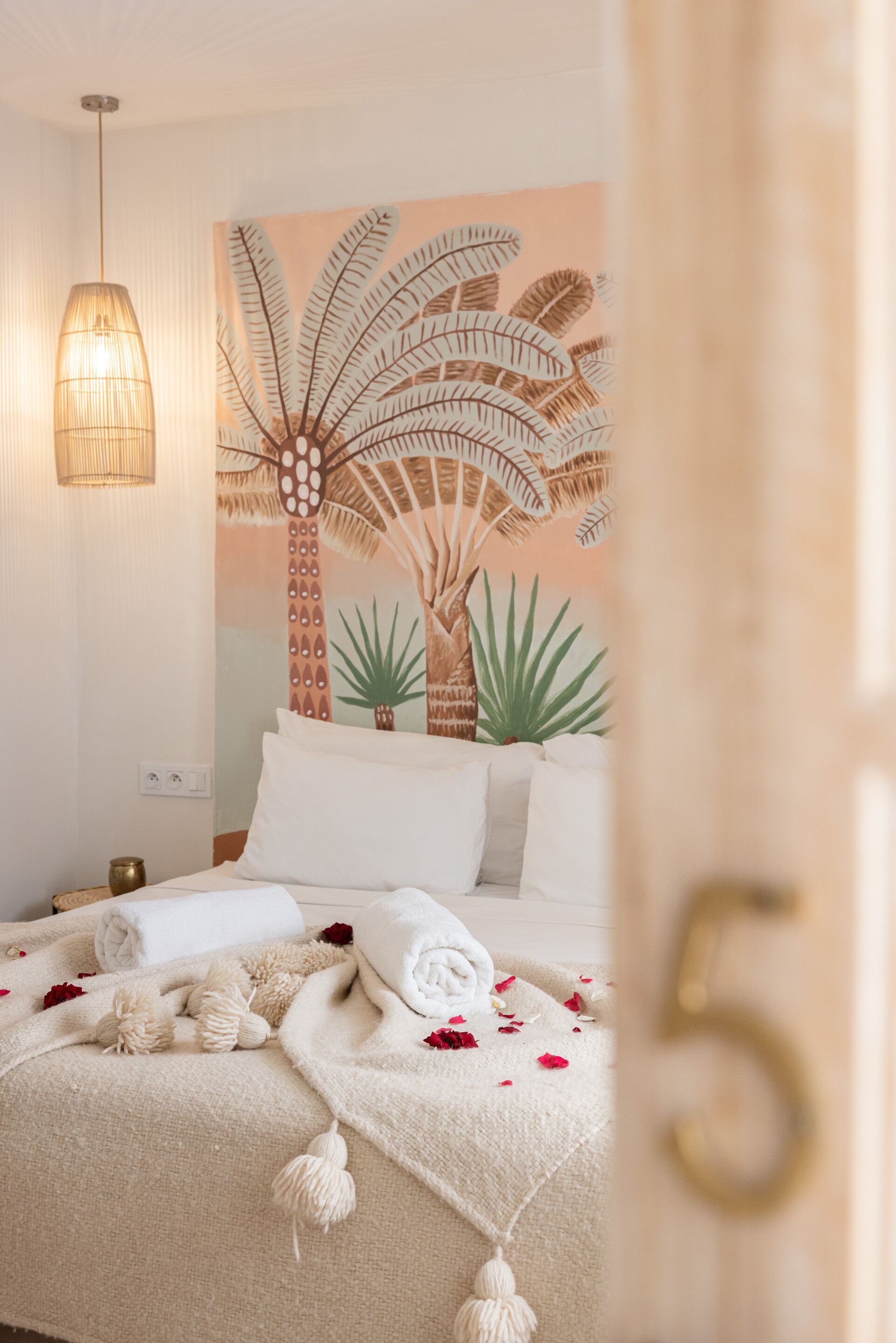 A bedroom with a bed, pillows, a blanket, and a wall with a palm tree mural.
