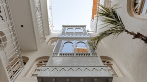 A high-ceilinged atrium with a central seating area, decorative ceiling patterns, and a view of a building with arched windows. - Riad k-white (Marrakech)