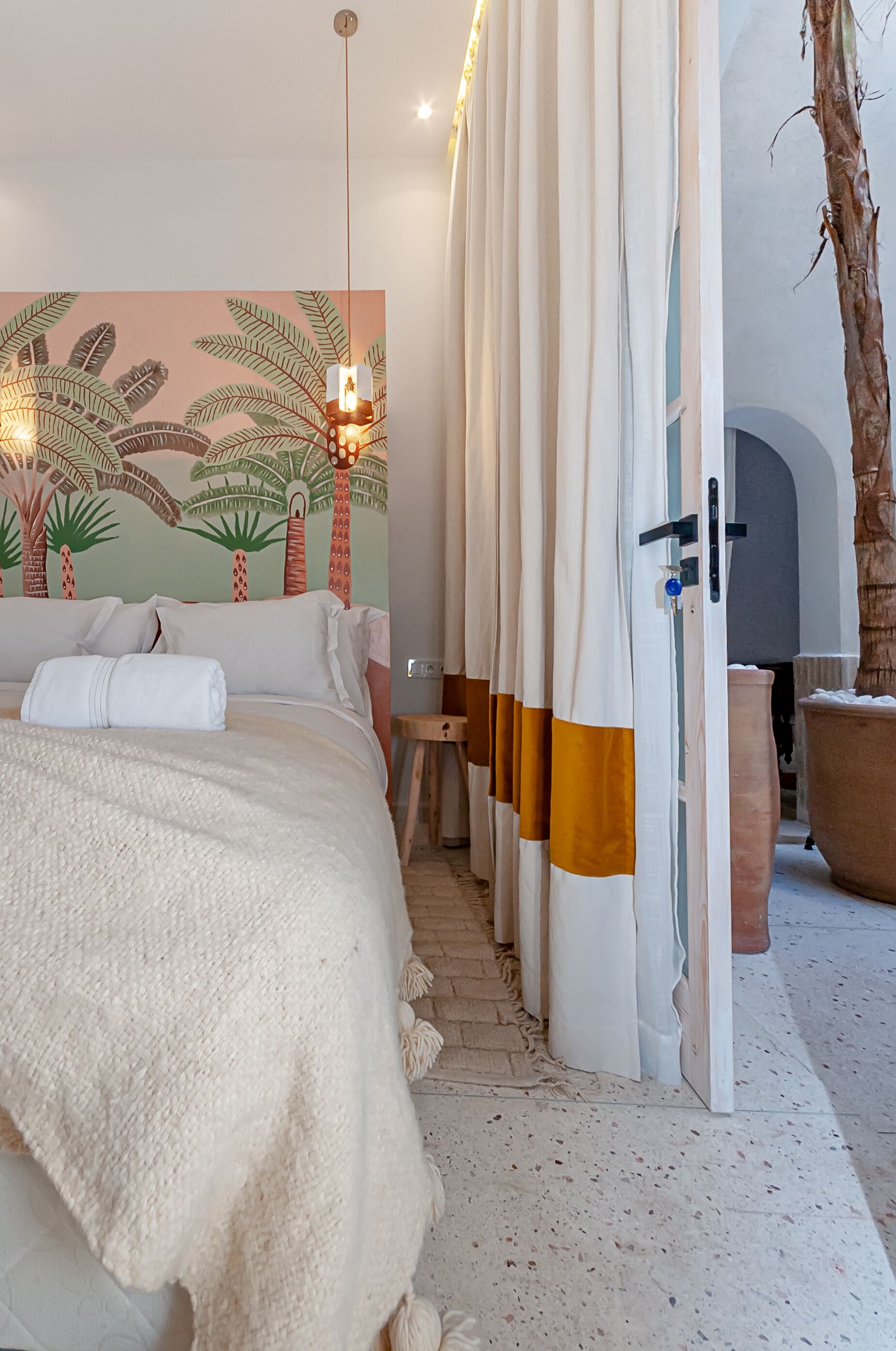 Een slaapkamer met een bed, wanddecoratie, gordijnen, een plant en een deur.