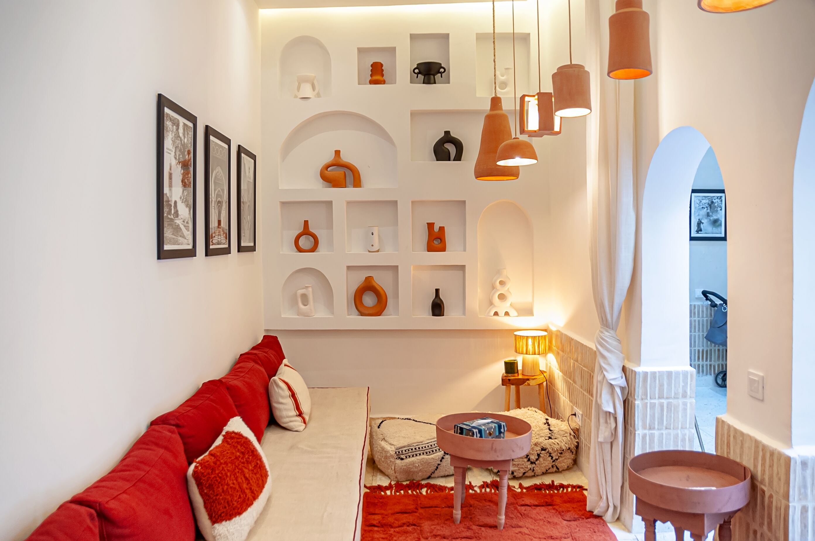Una sala de estar moderna con un sofá, cojines rojos, una mesita de centro y una estantería con diversos objetos decorativos.