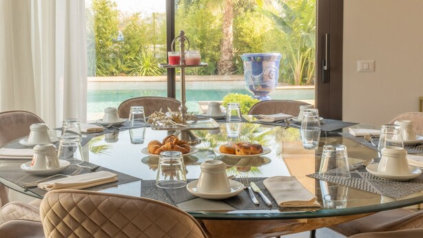 A dining table set for breakfast with pastries, a coffee pot, and a tea set, overlooking a pool and lush greenery. - Onda 8, Emma Villas - Four Bedroom Villa, Sleeps 8 (Scacciano)