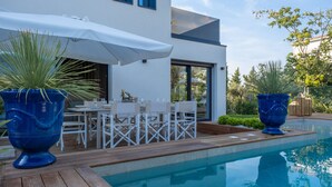 A modern outdoor dining area with a pool, white furniture, and large blue planters. - Onda 8, Emma Villas - Four Bedroom Villa, Sleeps 8 (Scacciano)