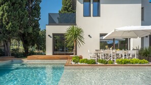 Una casa moderna con piscina, mobiliario de exterior y una palmera.