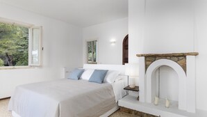 A bedroom with a bed, a nightstand, a fireplace, and a window with a view of trees. - Villa Meraviglia 8, Emma Villas (Nisporto)