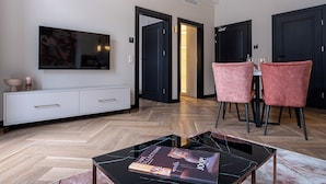 A modern living room with a white console, a glass coffee table, and a dining area with pink chairs. - Carvala Boutique Apartments (Czestochowa)