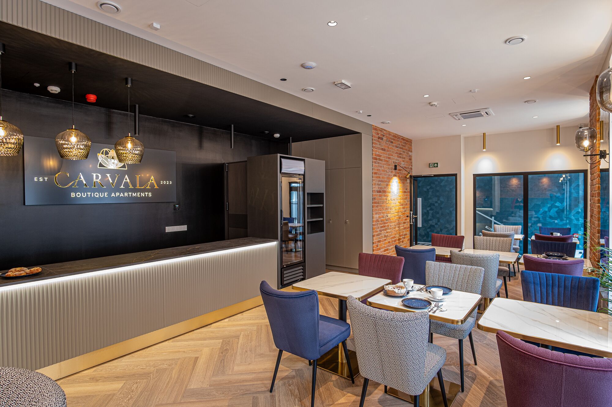 Un intérieur de restaurant moderne, avec un comptoir d’accueil, un espace salon et une vue sur l’extérieur.
