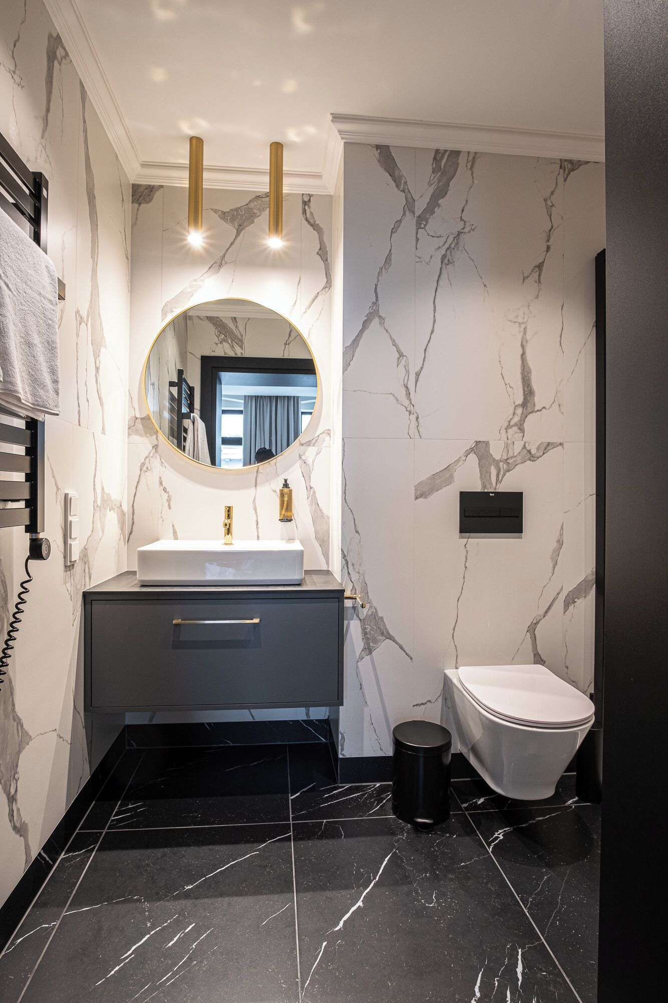 Een moderne badkamer met een marmeren wand, een ronde spiegel, een wastafel en een toilet.
