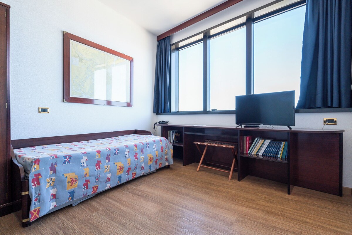 Een kamer met een bed, een bureau, een televisie en een raam met gordijnen.