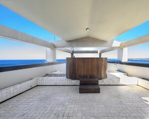 Une terrasse sur le toit avec un banc en bois, un sol carrelé de carreaux blancs et une vue sur la mer.